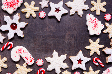 Christmas baking frame with a variety of red and white theme cookies and candies. Top down view on a dark stone background with copy space. Holiday candy cane baking concept.