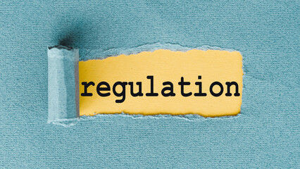The word regulation is written in black on a yellow piece of paper, which is partially torn to...