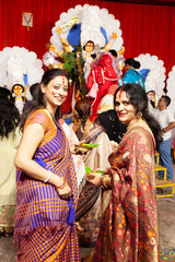 Naklejka premium Two joyful Indian women in traditional sarees performing the Bengali ritual 