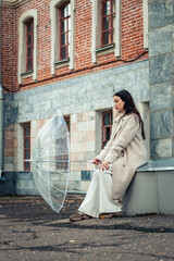 The girl sits with a transparent umbrella in her hands.