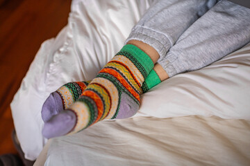 Women's feet in warm colored socks on a bed, close up