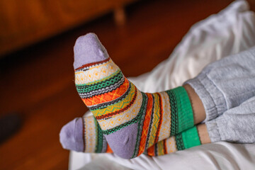 Women's feet in warm colored socks on a bed, close up