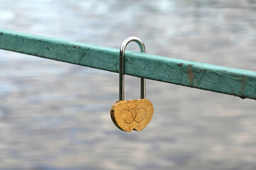 Alone golden pent padlock hangs on green metal bridge fence close up view