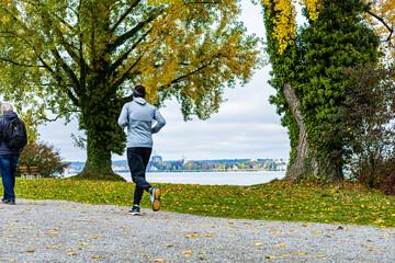 Fototapeta premium A man runs in a park with trees and a lake in the background. A woman is walking behind him