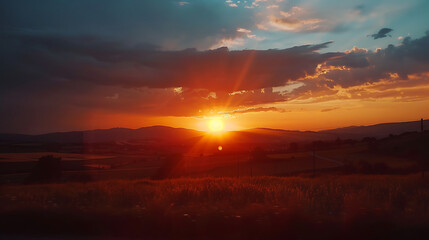 Fototapeta premium Orange sunset over a rural landscape with distant hills.