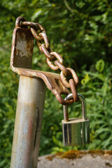 A padlock secured to a rusty chain and weathered metal pole