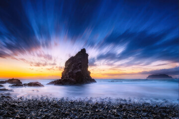 Long-exposure shot of a dramatic sunset over the ocean, with rocky formations and vibrant skies. Dynamic and captivating seascape. Generative AI