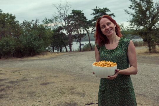 Young woman green dress holds a bowl of yellow berries alycha in her hands.