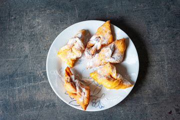 Hungarian crisp sweet pastry ¨csöröge fánk¨ (Angel Wings) with powdered sugar on a plate. 