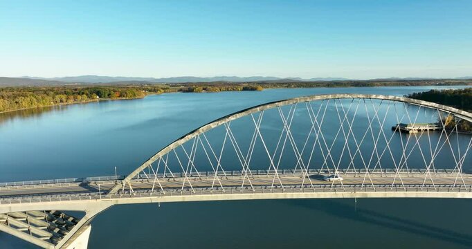 Aerial view of Lake Champlain Bridge during autumn, spanning the serene lake and connecting Crown Point, New York to Vermont, with fall foliage and distant mountain ranges under clear skies.