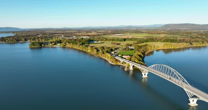 Aerial view of Lake Champlain Bridge during autumn, spanning the serene lake and connecting Crown Point, New York to Vermont, with fall foliage and distant mountain ranges under clear skies.