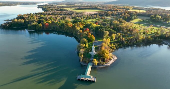 Aerial view of the Champlain Memorial Lighthouse on a small peninsula surrounded by calm water and vibrant autumn foliage.