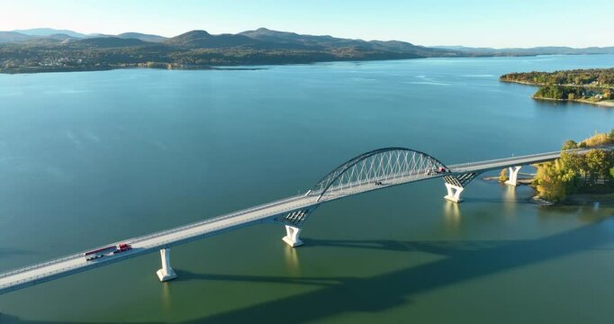 Aerial view of Lake Champlain Bridge during autumn, spanning the serene lake and connecting Crown Point, New York to Vermont, with fall foliage and distant mountain ranges under clear skies.