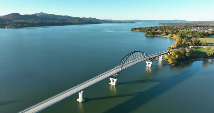 Aerial view of Lake Champlain Bridge during autumn, spanning the serene lake and connecting Crown Point, New York to Vermont, with fall foliage and distant mountain ranges under clear skies.