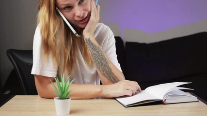 Woman Sits at Desk, Engaged in Phone Conversation While Jotting Down Notes. With Free Hand, Girl Gestures Animatedly, Balancing Work and Communication Seamlessly