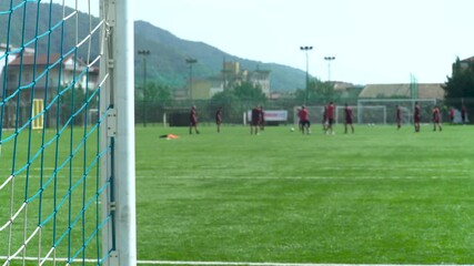 Soccer field, goal net in the foreground with players training in the background