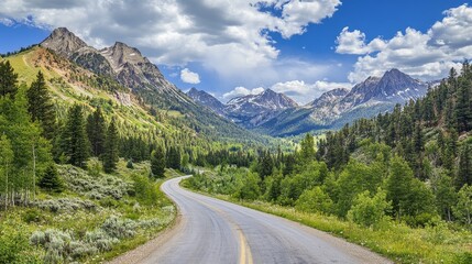 Obraz premium A serene mountain road curves gently through lush greenery beneath a vast blue sky