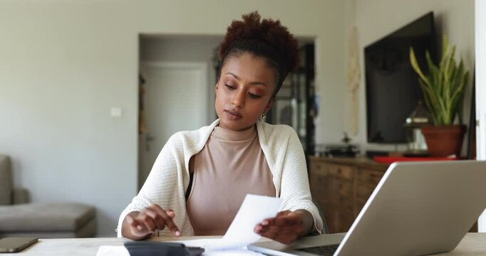 African woman sit at desk with laptop engaged in expenses and incomes calculations, review family expenses, budgeting, analyze financial data, do accountancy job from home office. Finances management