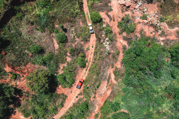 Car driving on a dirt road in a forest. The road is bumpy and rocky, and the trees are lush and green.
