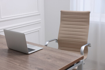 Beige leather chair, laptop and desk in office