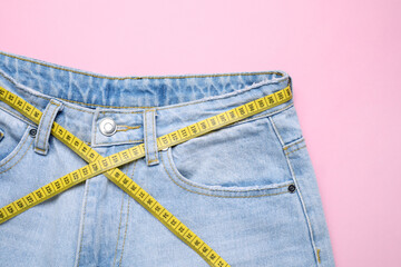 Jeans and measuring tape on pink background, top view