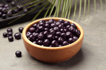 Ripe acai berries in bowl on grey textured table, closeup