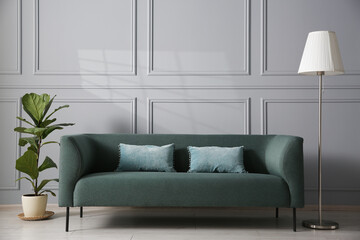 Comfortable sofa, houseplant and lamp near grey wall in room
