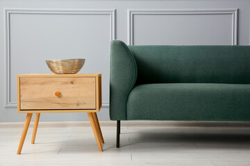 Stylish sofa and bowl on side table near grey wall