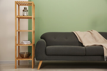 Stylish sofa with blanket and shelving unit near green wall indoors