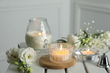 Beautiful burning candle and flowers on white wooden table