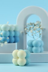 Beautiful bubble candles, gypsophila flowers and geometric figures on light blue background, closeup
