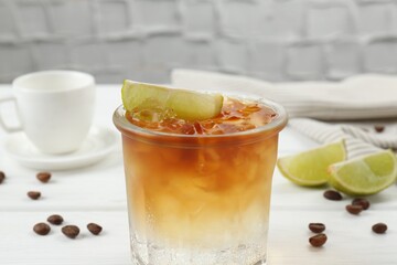 Refreshing espresso tonic drink with slice of lime and coffee beans on white wooden table, closeup