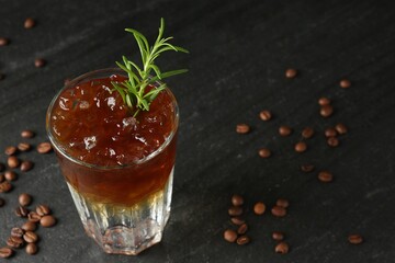 Refreshing espresso tonic drink with rosemary and coffee beans on dark table, closeup
