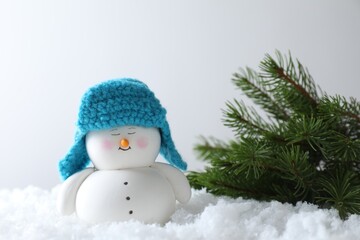 Cute decorative snowman and fir branches on artificial snow against light background