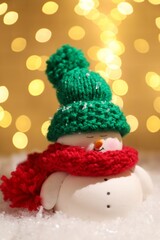 Cute decorative snowman on artificial snow against blurred lights, closeup