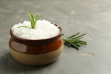 Sea salt in bowl and rosemary on grey table, closeup. Space for text