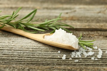 Sea salt in spoon and rosemary on wooden table, closeup