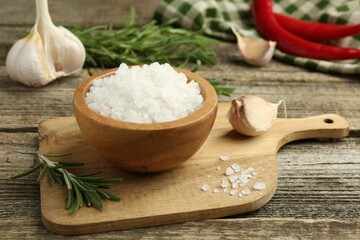 Sea salt in bowl, rosemary and garlic on wooden table, closeup