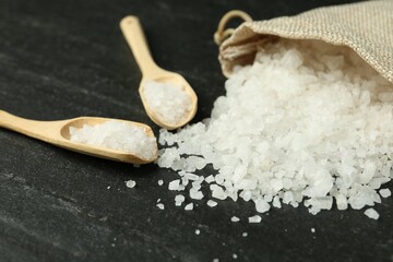 Sea salt, bag and spoons on dark gray textured table, closeup