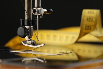 Professional sewing machine and measuring tape on black background, macro view