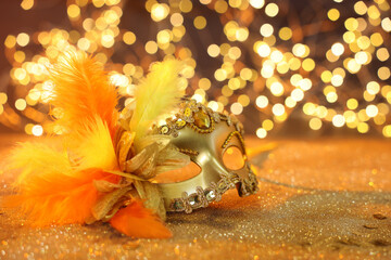 Beautiful carnival mask on golden shiny background, space for text. Bokeh effect