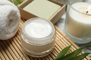 Spa composition with different cosmetic products, burning candle and leaves on white marble table, closeup