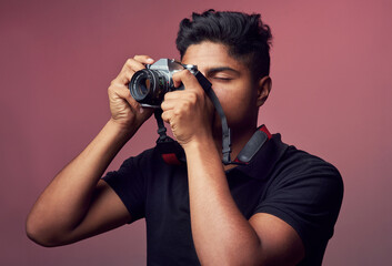 Studio, asian man and photography with camera for shooting, sightseeing or capture picture with lens. Career, male person and journalist with equipment for photographer, production or pink background