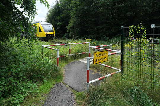 Umlaufgitter an Bahn&uuml;bergang f&uuml;r Fu&szlig;g&auml;nger mit Zusatzschild Radfahrer absteigen und herannahender Zug - Stockfoto