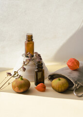 A composition of aroma oil in frosted bottles on a light background, next to which lies a fig, a physalis, a bag and a dried flower
