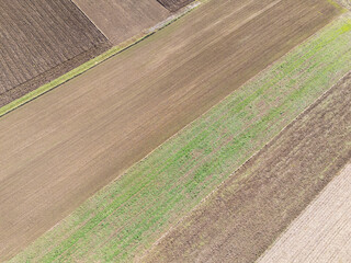 Aerial view of recently plowed agricultural fields showing various soil textures and colors. The...