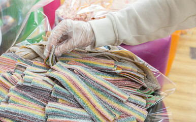 A gloved hand carefully arranges colorful gummy candy in a clear bag. The gummies are in a rainbow...