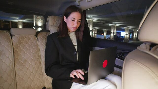 A professional woman is diligently working on her laptop inside a car during nighttime, perfectly blending her business and lifestyle needs
