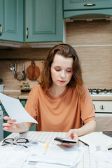 woman pays bills online, sits in kitchen with receipts and calculator. Online banking at home...