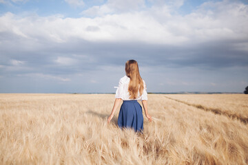 portrait of a Young beautiful free woman with long blond hair and a blue skirt in a field of wheat in sunny day